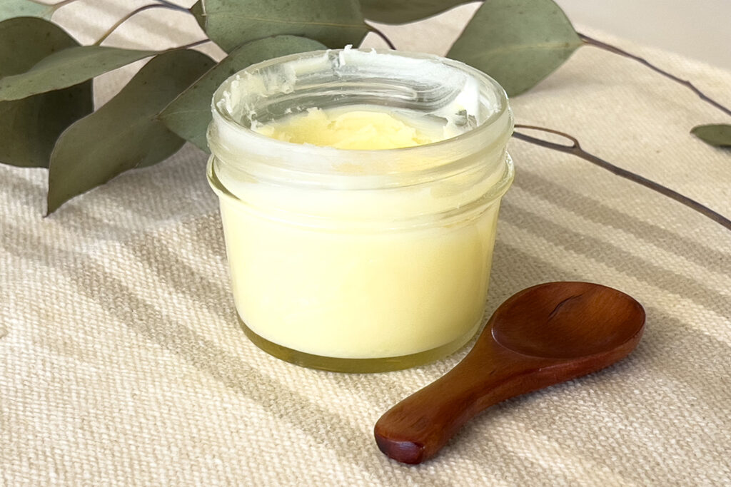 jar of diy moisturizer sits on a cloth with a wood spoon next to it