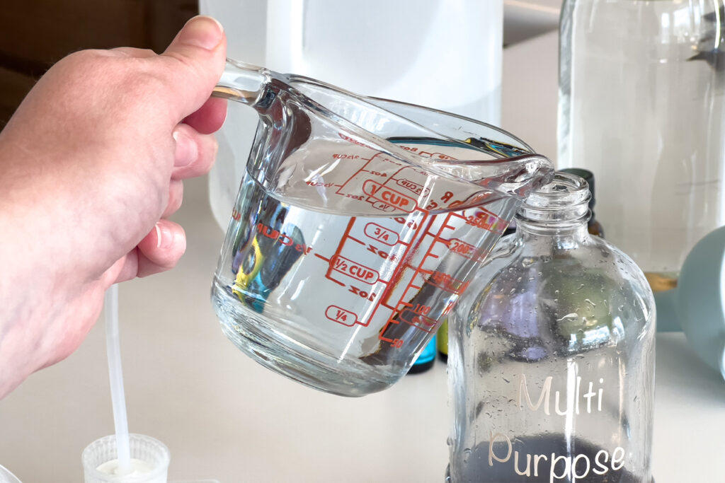 a measuring cup that is pouring vinegar into a spray bottle for how to make a multi purpose cleaning spray