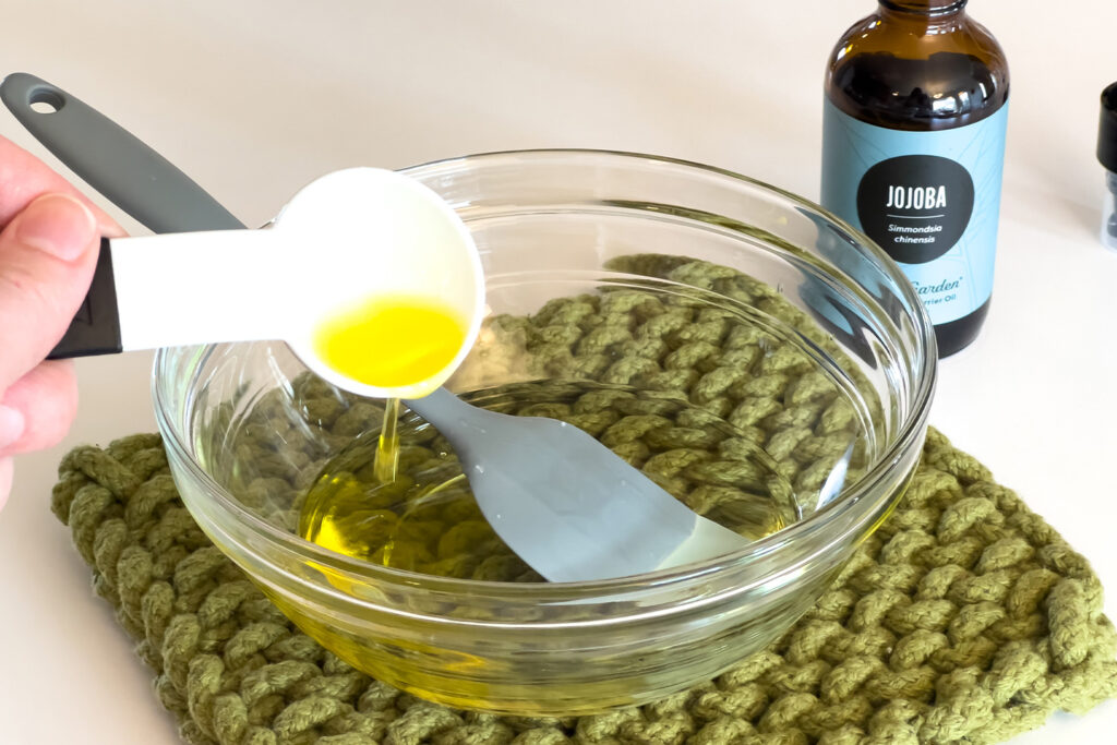 jojoba oil is being added to a bowl of melted shea butter to make the diy face moisturizer