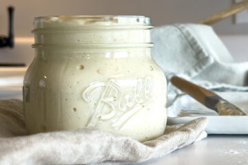 a jar of sourdough starter sits on the kitchen counter on a linen cloth