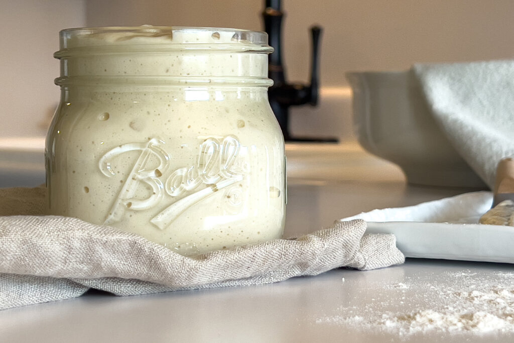 a jar of sourdough starter sits on the kitchen counter on a linen cloth