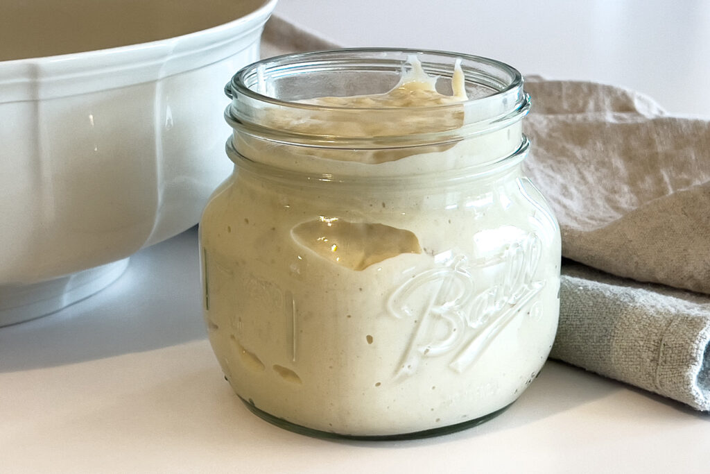 a jar of sourdough starter sits on the kitchen counter next to a mixing bowl, for why sourdough starter