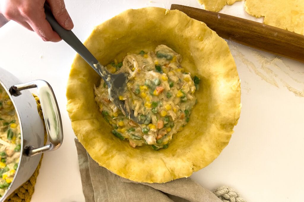 a woman is scooping chicken pot pie filling into the best sourdough pie crust