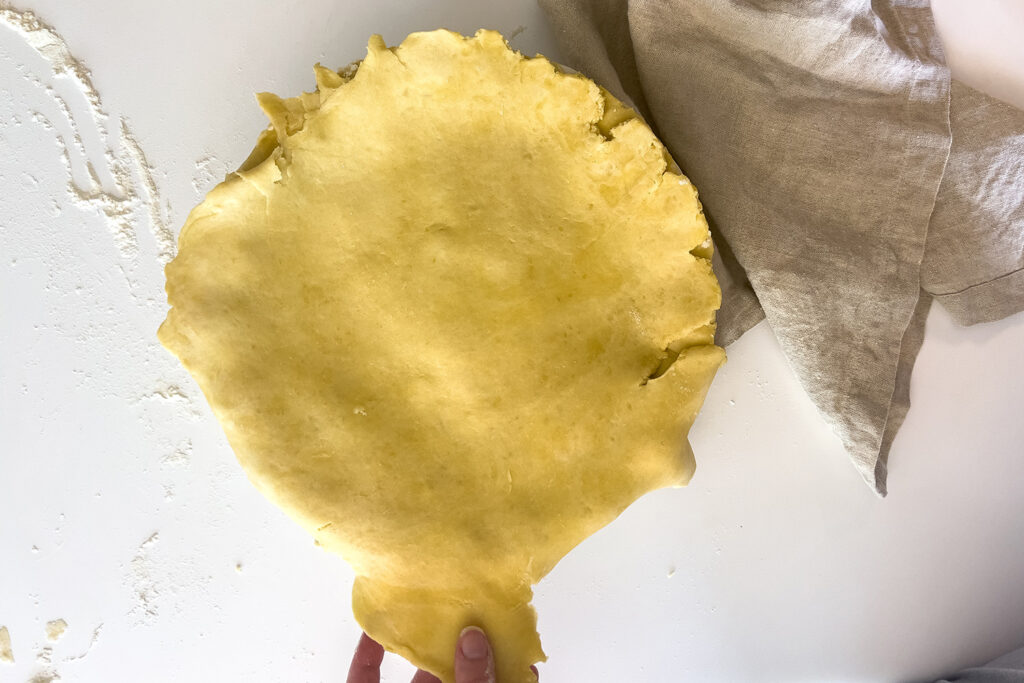 a woman is laying pie crust over the top of the rest of the dough
