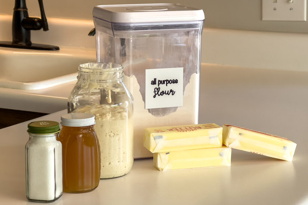 salt, honey, a sourdough starter, flour, and butter sit on the kitchen counter
