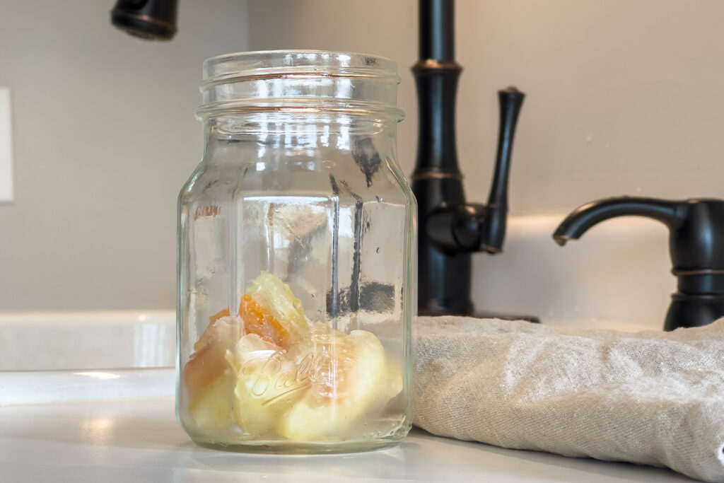 a jar of diy vinegar garbage disposal cleaner pods sits next to the sink
