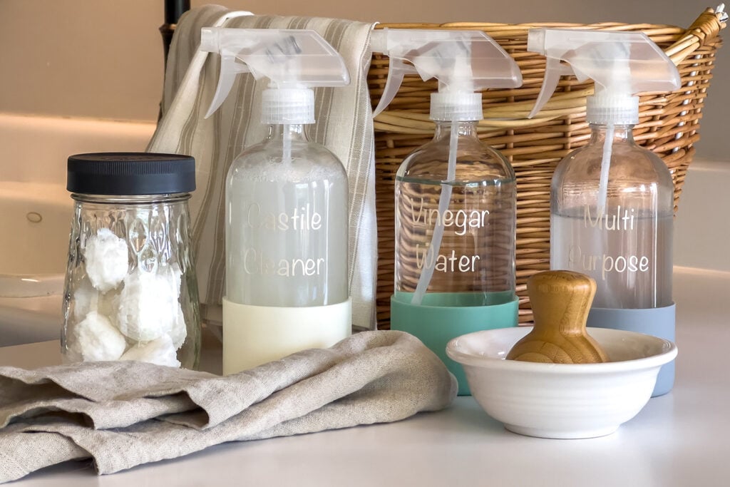 a jar of diy garbage disposal cleaning pods, a bottle of Castile Cleaner Spray, a bottle of vinegar cleaning spray, and a bottle of multi purpose cleaning spray sit next to each other