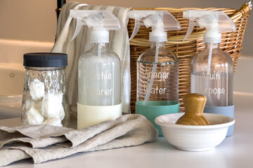 a jar of diy garbage disposal cleaning pods, a bottle of Castile Cleaner Spray, a bottle of vinegar cleaning spray, and a bottle of multi purpose cleaning spray sit next to each other