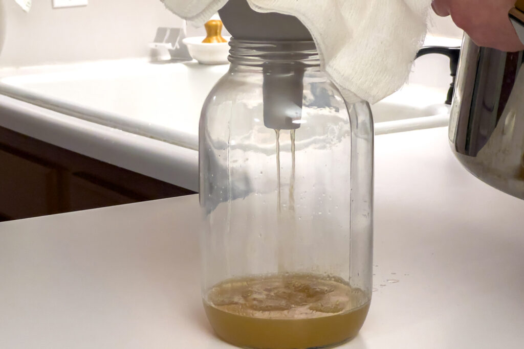 bone broth is being poured into the jar through the funnel and cheesecloth
