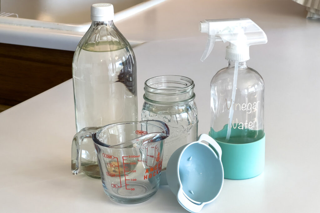 distilled vinegar, water, a spray bottle, a funnel, and a measuring cup sit on the counter