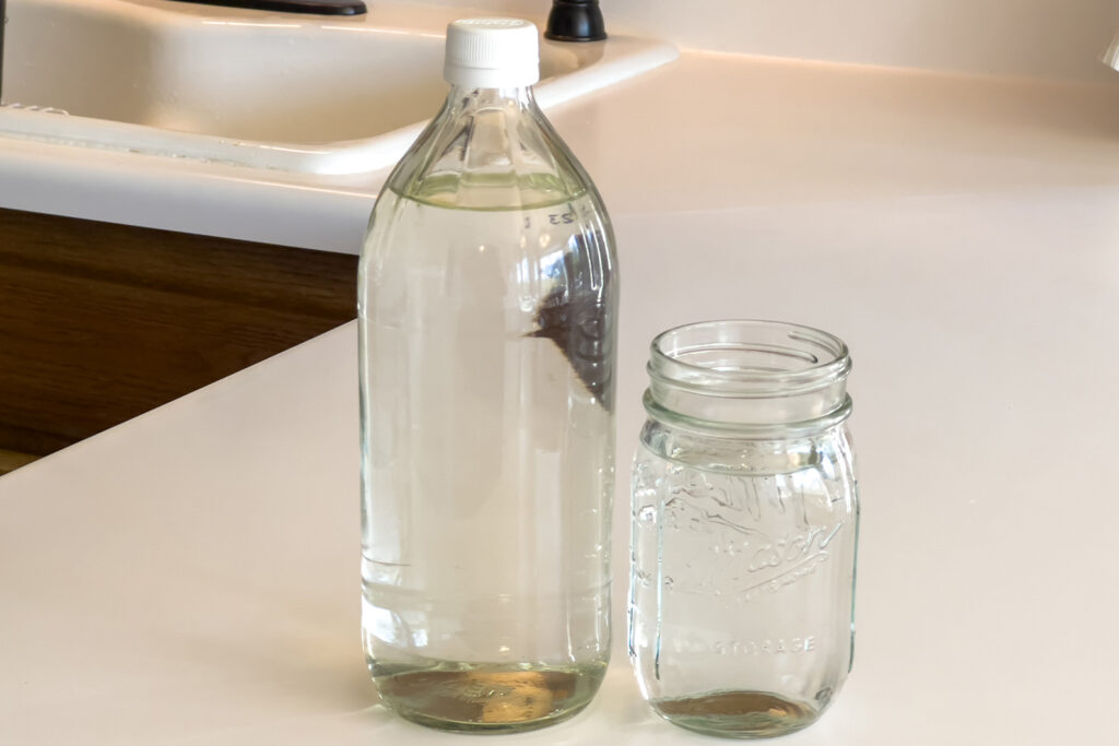 distilled white vinegar and a jar of distilled water sit on the kitchen counter, both ingredients of the homemade vinegar water cleaning spray