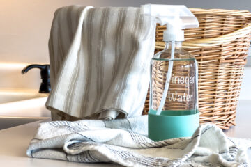 a vinegar water cleaning spray sits on the kitchen counter next to cleaning supplies