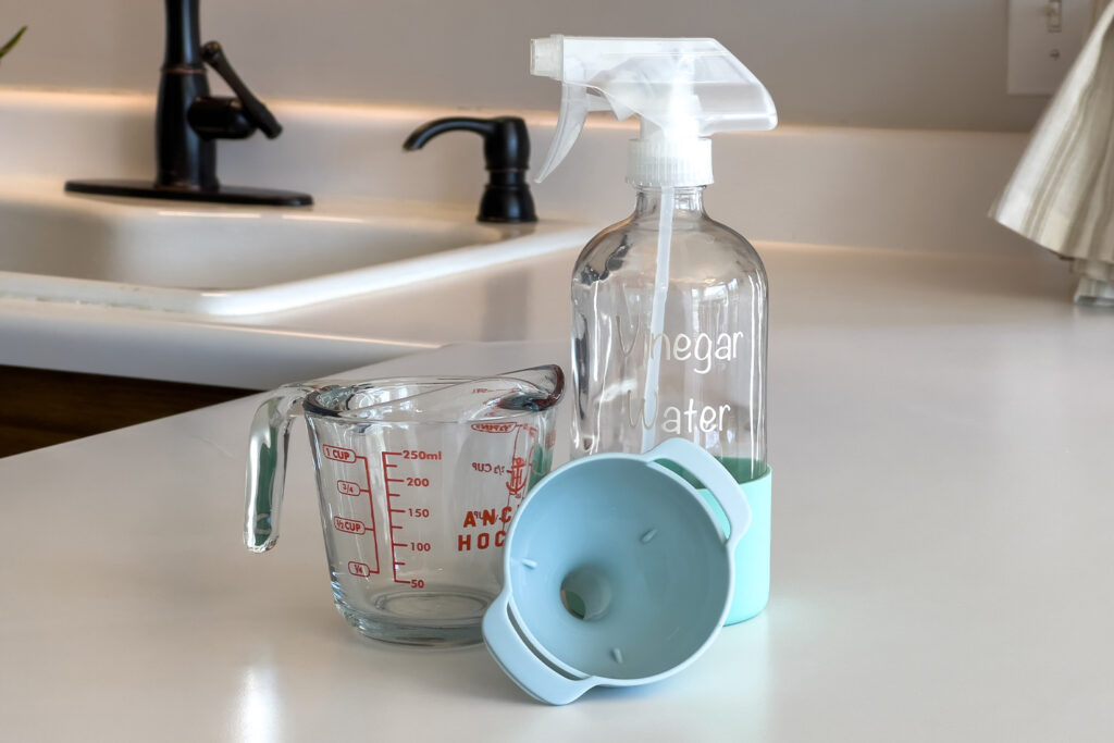 a measuring cup, a spray bottle, and a funnel sit on a kitchen counter
