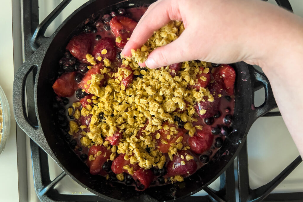 a woman is sprinkling a crumble topping on top of a lemon berry filling in a cast iron skillet