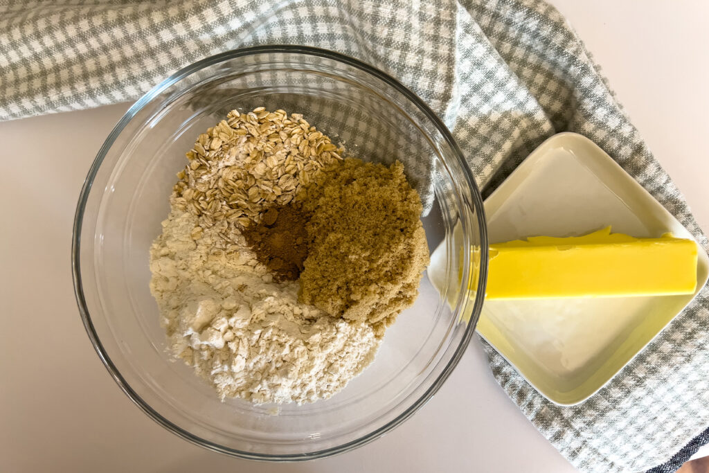 a bowl of crumble topping ingredients sits next to a stick of butter