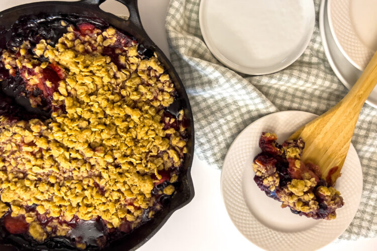 a cast iron skilled filled with lemon berry crumble cobbler sits on the kitchen counter next to some plates