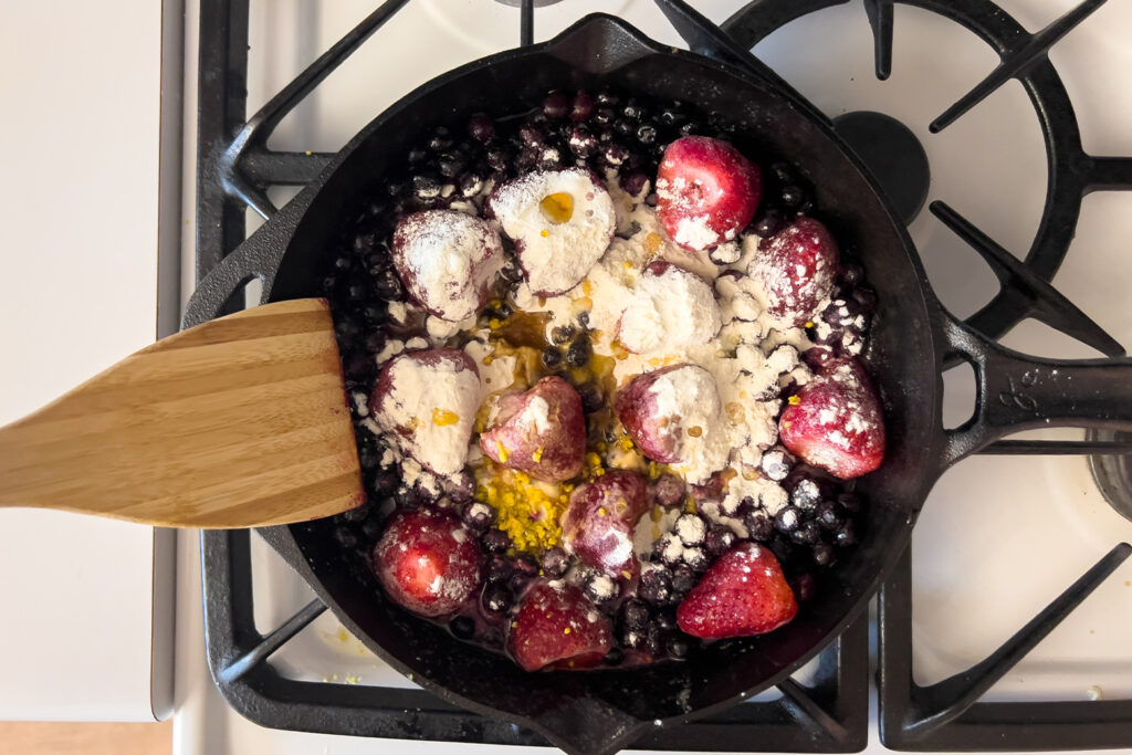flour and lemon zest are being poured over the berries in a cast iron skillet