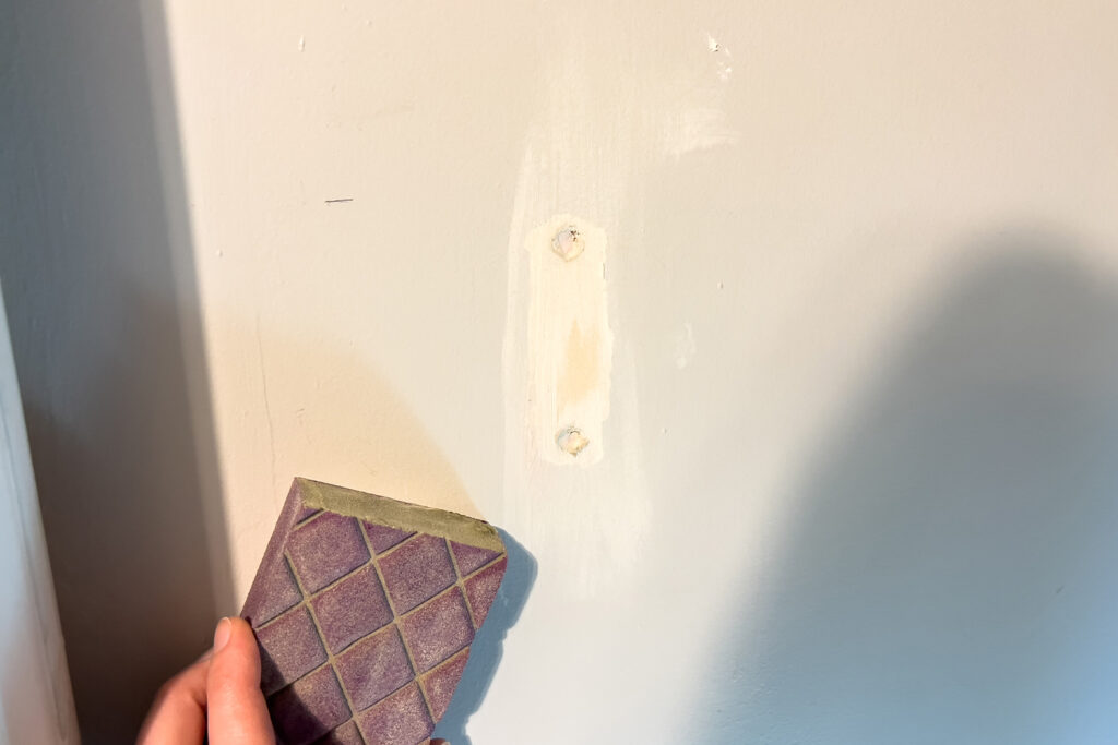 woman sanding spackeling on the wall during this budget friendly pantry renovation