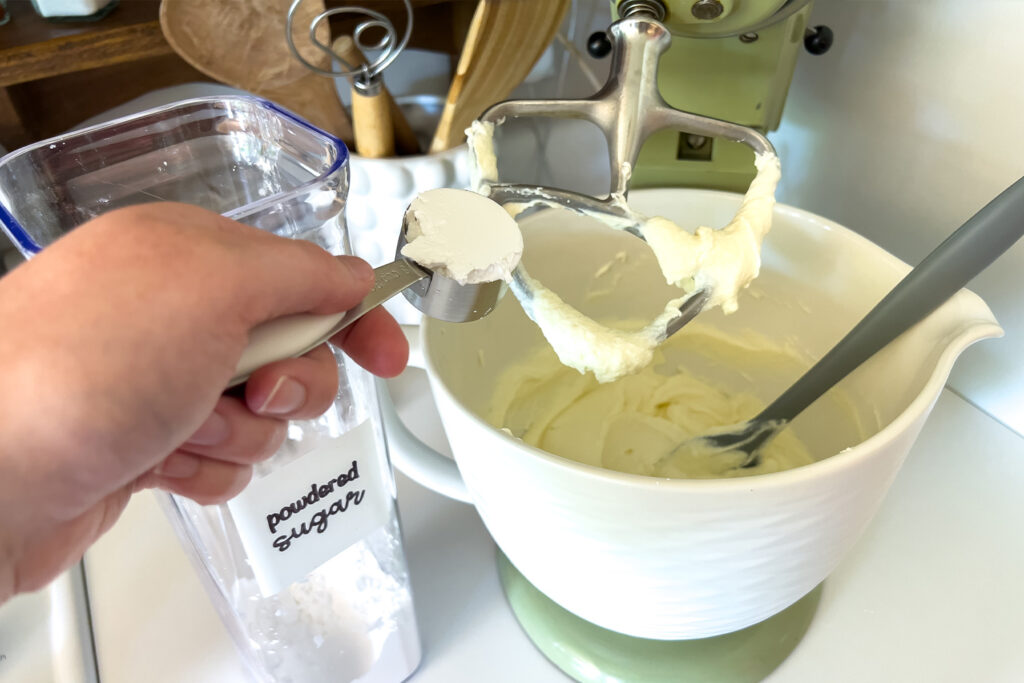 a woman adding powdered sugar to the bowl of her stand mixer
