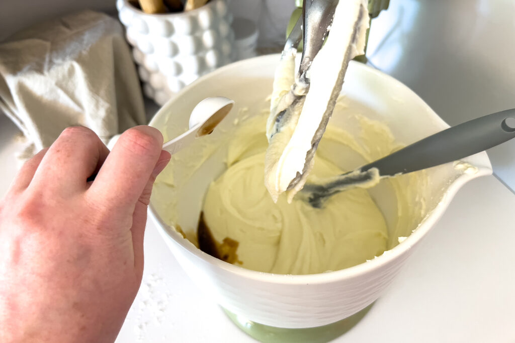 a woman adding vanilla extract to the bowl of her stand mixer