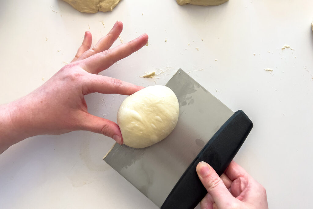 a woman lifting a dough ball with a pastry cutter