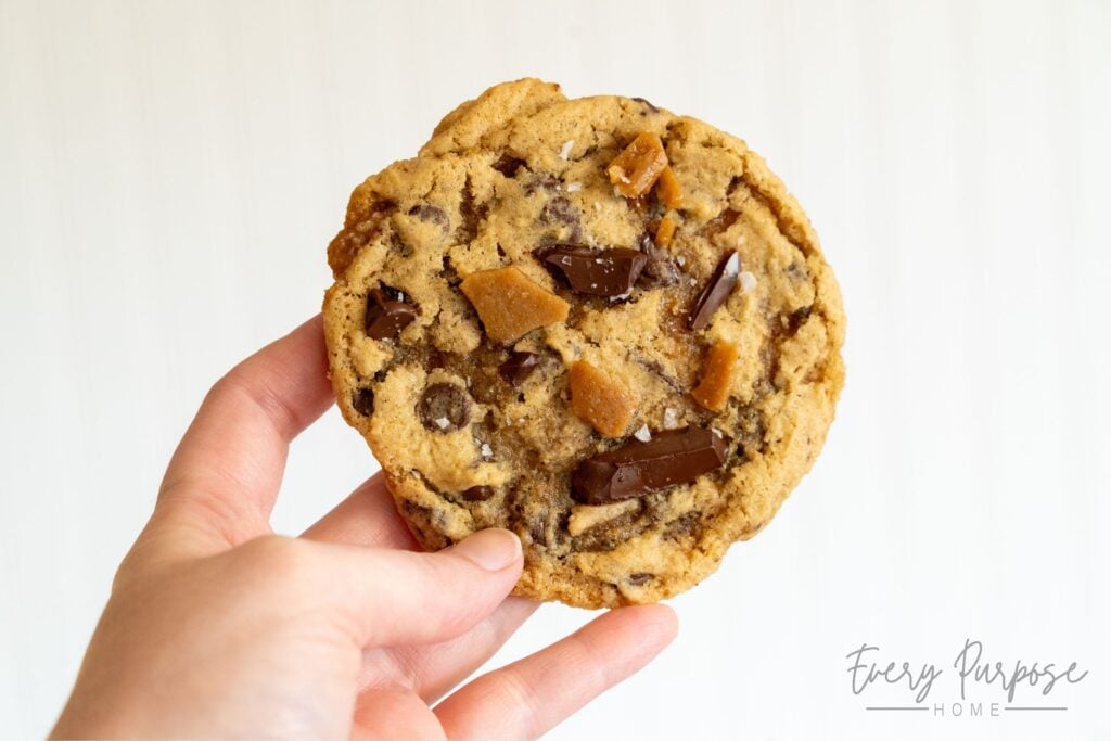 holding a large bakery style sourdough toffee chocolate chip cookie
