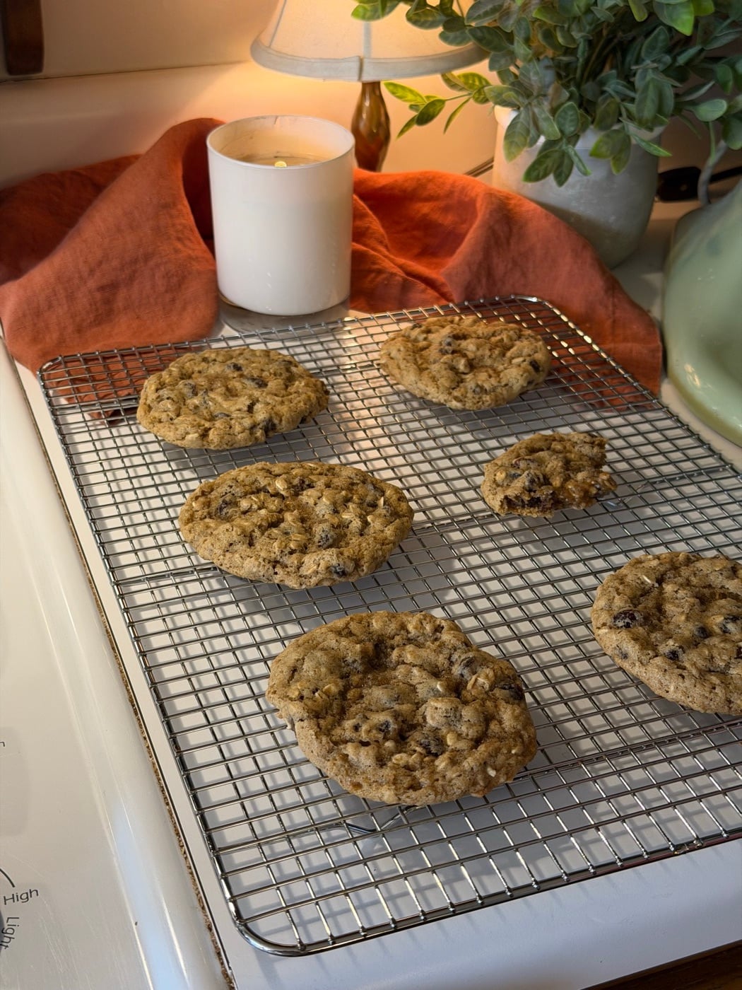 Sourdough oatmeal cookies cooling on a rack beside a candle and a warm lamp
