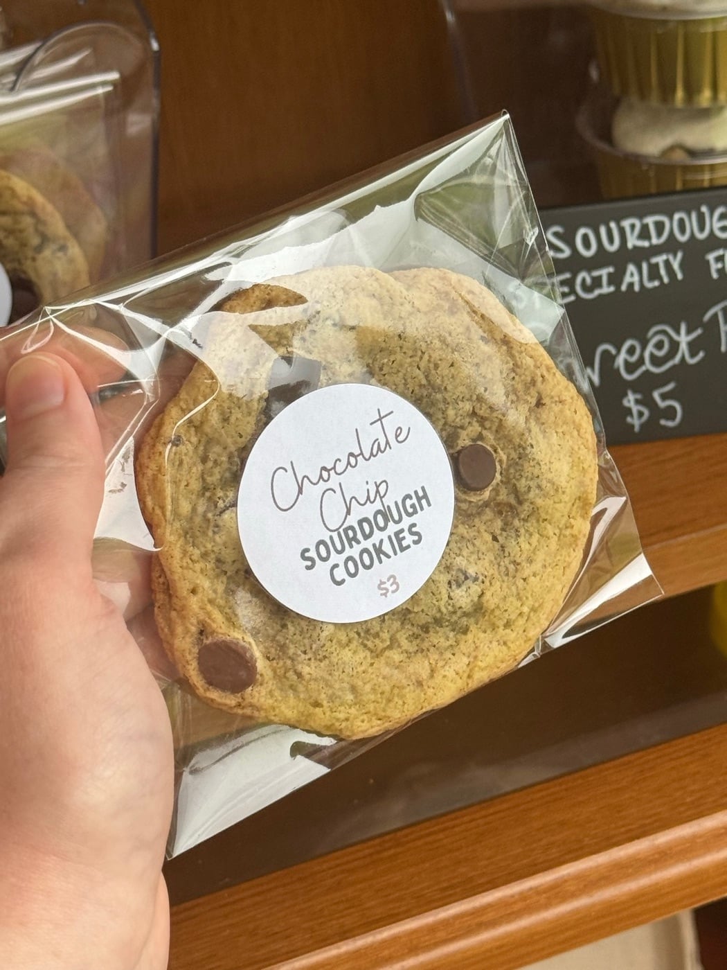 A wrapped chocolate chip sourdough cookie with a handwritten label