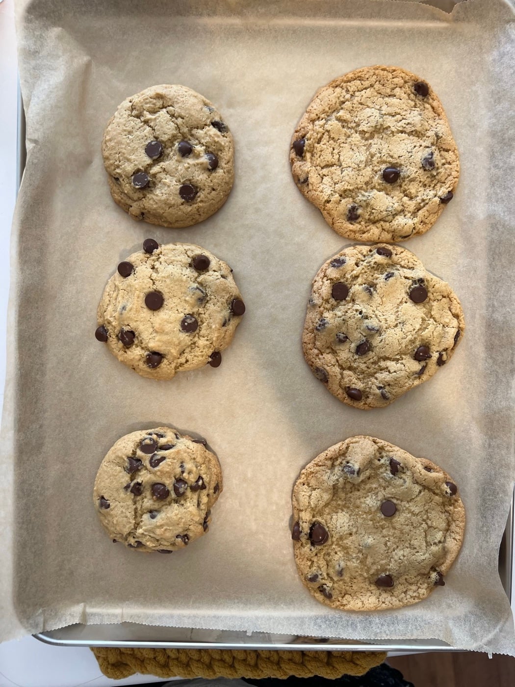 A sheet pan of six test batches of sourdough chocolate chip cookies side by side
