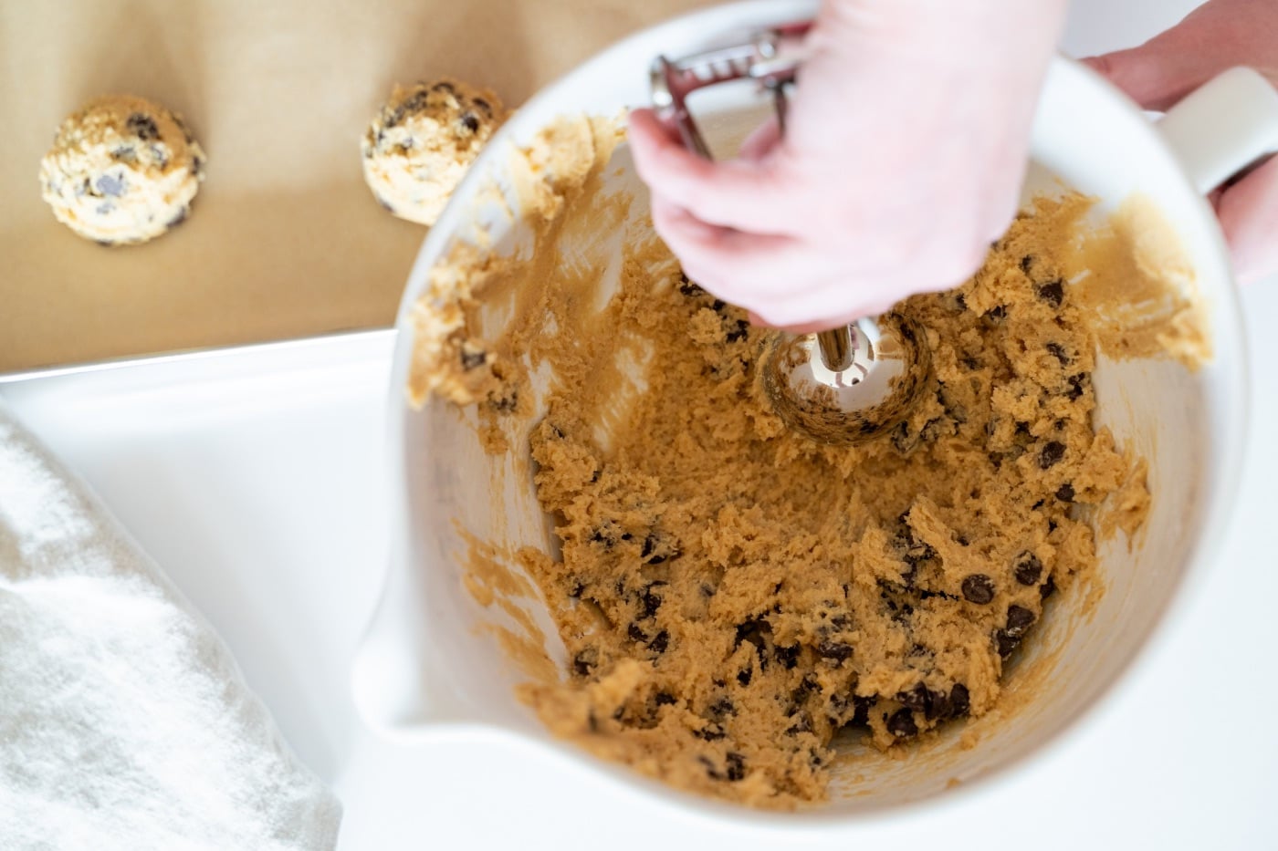 Marlene scooping sourdough chocolate chip cookie dough from her mixing bowl onto a parchment-lined pan