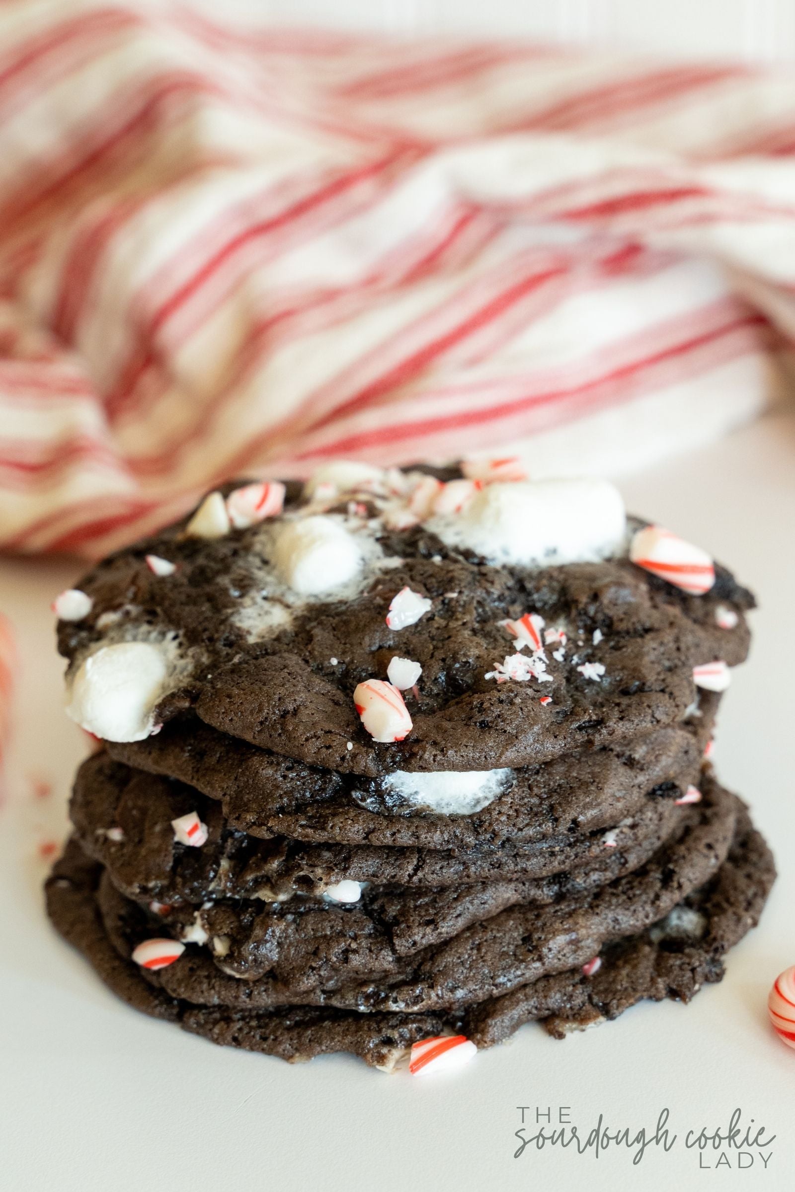 A stack of thick sourdough peppermint hot cocoa cookies topped with melty marshmallows and crushed candy canes.